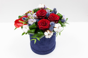 A bright bouquet of red flowers (rose and anthurium) with green leaves, Alstroemeria and cotton flowers in a blue box for hats on a light background