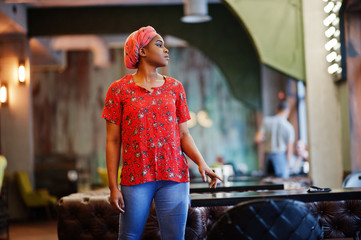 Wall Mural - Stylish african woman in red shirt and hat posed indoor cafe.