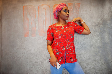 Wall Mural - Stylish african woman in red shirt and hat posed against wall with rock sign.