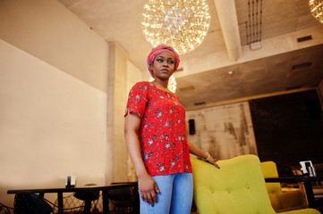 Wall Mural - Stylish african woman in red shirt and hat posed indoor cafe.