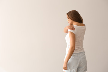 Poster - Young woman suffering from pain in shoulder on light background