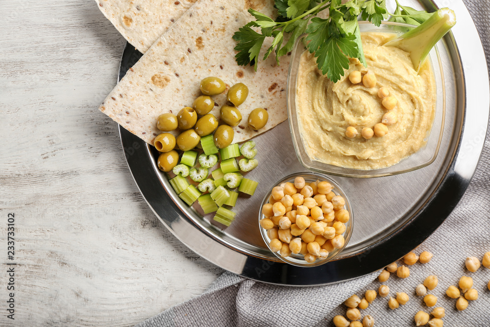 Bowls with tasty hummus, chickpeas and flatbread on metal tray