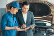 Male customer signing a document while auto mechanic explaining something to him in car service