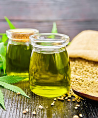 Oil hemp in two jars and flour in spoon on wooden board