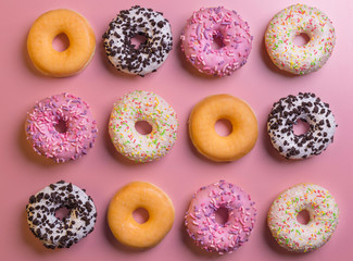 Top view of many colorful donuts on pink background.