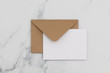 © ink drop - Blank white card with kraft brown paper envelope on marble background