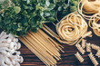 Different types of  uncooked pasta on wooden background. Fettuccine, spaghetti and fusilli with shimeji mushrooms and basil. Food background.