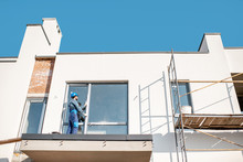 White Building Facade With Workman In Uniform Mounting The Window On The Balcony
