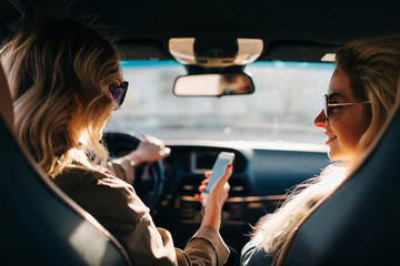 Photo of back of two women with long hair and phone in hand sitting in car