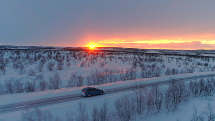 Wall Mural - AERIAL: Car driving on snowy highway through scenic winter country at sunset