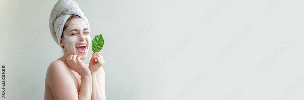 Beauty portrait of woman in towel on head with white nourishing mask or creme on face and green leaf in hand, white background isolated. Skincare cleansing eco organic cosmetic spa concept Banner - obrazy, fototapety, plakaty 