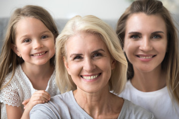 Wall Mural - Smiling senior grandmother looking at camera with young daughter and kid granddaughter at background, older grandma in three 3 women happy loving family, older elderly generation concept, portrait