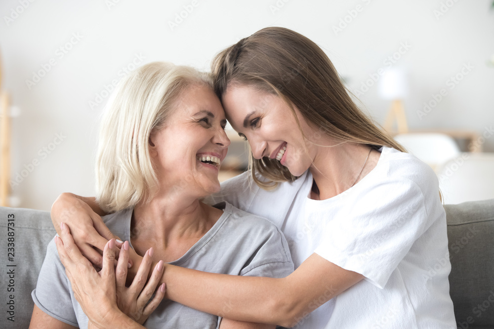 Happy loving older mature mother and grown millennial daughter laughing embracing, caring smiling young woman embracing happy senior middle aged mom having fun at home spending time together - obrazy, fototapety, plakaty 