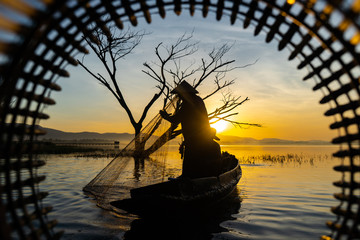 Fishermen in a boat catching fish in the reservoir in the early morning sunrise.