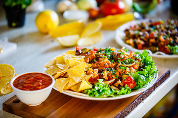 Grilled meat with nachos and vegetables on wooden background