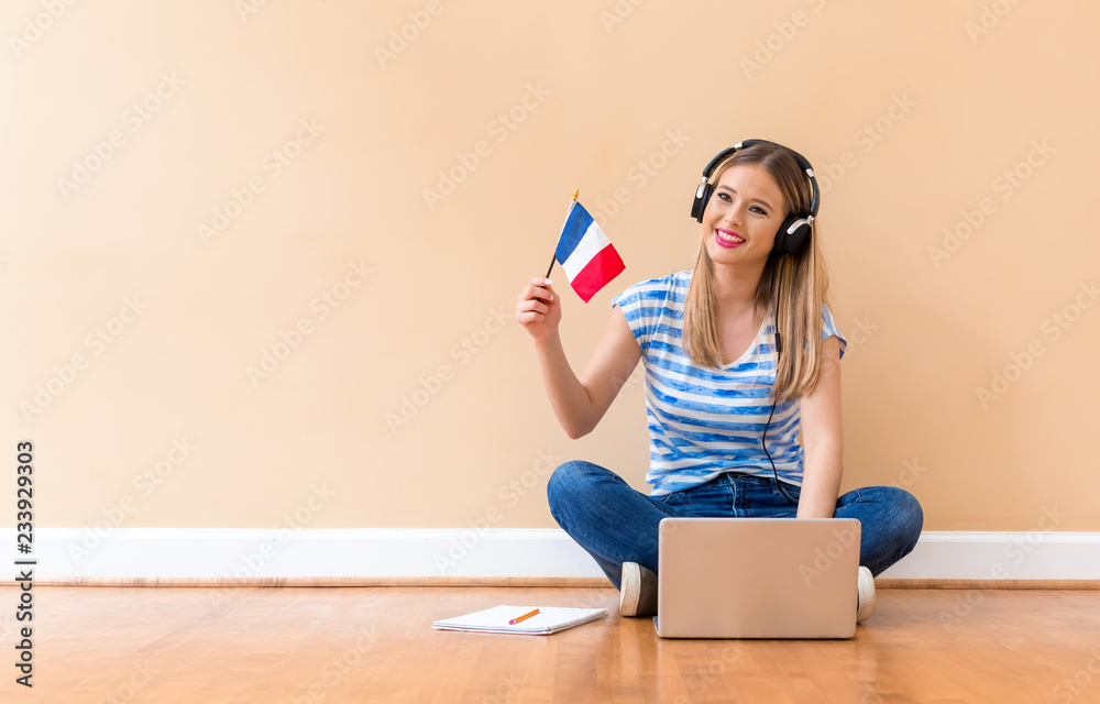 Young woman with French flag using a laptop computer against a big interior wall - obrazy, fototapety, plakaty 