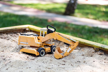 Yellow Excavator Toy In Wooden Sandbox At Yard. Boy's Toys Concept