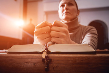 Wall Mural - Christian woman praying in church. Hands crossed and Holy Bible on wooden desk.