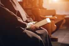 A Monk In Robes With Holy Bible In Their Hands Praying In The Church