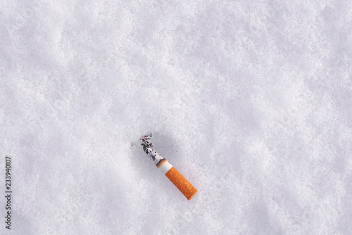 Fotografija top view of smoking cigarette butt on a snow with copy space