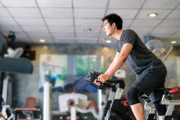 Asian man exercising on stationary bike at gym.