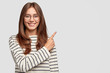 © wayhome.studio  - Waist up shot of pretty Caucasian woman with cheerful expression, points with index finger at blank copy space, dressed in striped sweater, shows free space at upper right corner for your promotion