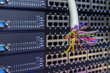 A damaged telephone cable is located on the background of empty server hardware ports. Multicolored wires are located near the Internet switch. The concept of a connection failure