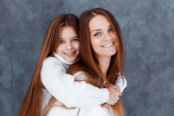 Stylish beautiful mother and a cute daughter with blue eyes in studio hugging and having fun. family, love concept