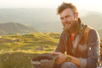 Close-up portrait of a bearded stylish traveler in a cap against epic rocks. Time to travel concept