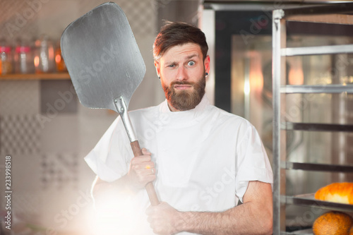 Fotografía A young funny baker with a pizza spatula in his hands against the backdrop of an