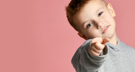 Young boy kid in grey hoodie pointing one finger at the corner smiling isolated on pink 