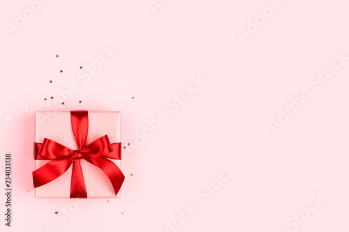 The pink gift box with red bow on the pink background with golden sparkles. M...