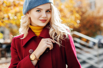 Happy smiling girl wearing burgundy, marsala coat, blue beret, yellow turtleneck, golden wrist watch, hoop earrings posing in street. Autumn fashion, advertising concept. Copy, empty space for text