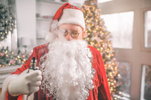 Relaxed Man In Santa Claus Costume Stands And Holds Vape In Hand. Smoke Comes Out Of His Mouth. He Is Relaxed.