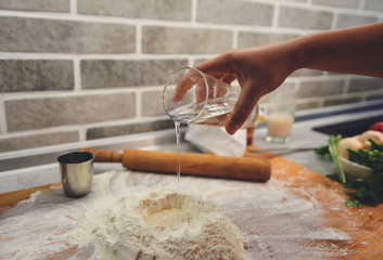 A hand with a glass adds water to the flour.