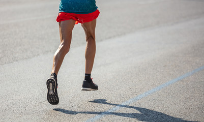 Wall Mural - Running in the city roads. Young man runner, back view, blur background, copy space