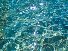 Blue Transparent Water Surface With Bright Sun Glare And Sunny Shining Reflections On Bottom. Top View Of Turquoise Ripple Texture With Sunlight Refracting Through Liquid Layer.