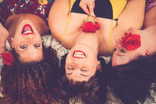 Three Young Women Have Fun Together Laying On The Bed At Home Laughing A Lot And Having A Lot Of Fun - American Style With Red Roses And Big Smiles For Nice And Cute People