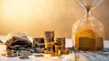 Sand running through the shape of hourglass with banknotes and coins stack of international currency on table. Time investment. retirement saving. Urgency countdown timer for business deadline concept