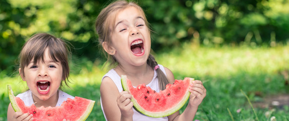 two little cute girls eating watermelon outdoors