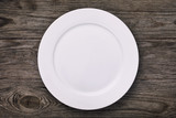 Fototapeta  - White empty ceramic plate on wooden table, top view. Food background