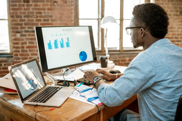 Wall Mural - young african man working with analitycs sitting at the beautiful working place with computer, lapto