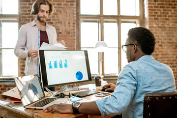 Wall Mural - Two male coworkers working with analitycs in the beautiful office with brick wall on the background