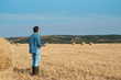 Man farmer agronomist in jeans and shirt stands back in the field after haymaking, with tablet looking into the distance. Rural business, agricultural industry, freedom after work, concept