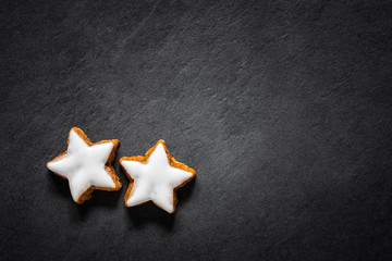 Two fresh cinnamon star shaped cookies with frosting on black slate background