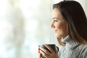 Wall Mural - Happy woman looking to rain holding coffee through the window