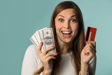 Wall Mural - beautiful young girl holding dollars in her hands and a credit card on a blue background