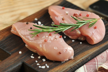 Chicken breast fillet on a dark wooden tray. Raw meat supplemented with a sprig of rosemary and spices. Close-up. Macro shooting.