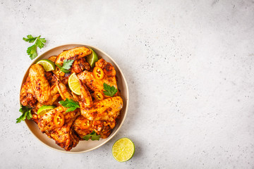 Spicy grilled chicken wings in tomato sauce in a white plate on a white background.