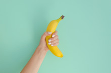 Female Hand Holding A Banana On A Mint Background. Minimal Fruit Concept.